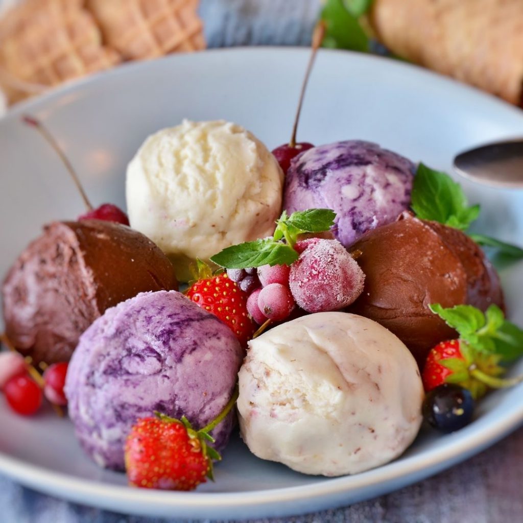 6 scoops of ice cream and sorbet (chocolate, vanilla, berry) arranged alternatingly in a circle on a white plate with frozen strawberries in the centre
