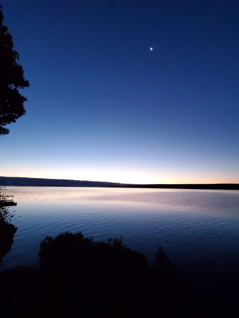 sunrise over a lake with a crescent moon in the sky